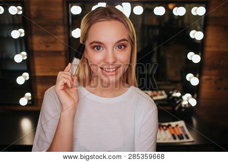 Nice Beautiful Young Woman Look On Camera And Pose. She Hold Lipgloss In Hand. Woman In Beauty Room.