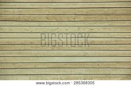 The old wall of planks is covered with peeling paint of yellow-brown color