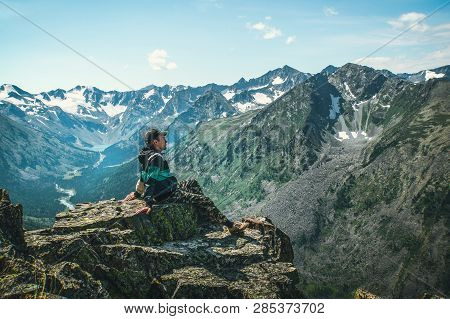 Man Sit On Sharp Cliff Above Valley In Rocky Mountains Park And Watch Into Landscape. The Tourist Ha