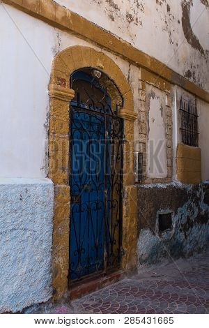 Street With A Detail Of An Old House. Bright Blue Door, Iron Ornate Grating And A Yellow Frame. Safi