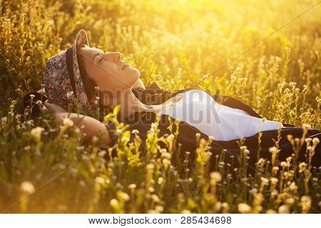 Happy Girl In A Hat Is Lying Among Wild Flowers And Dreaming About Something