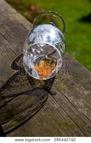 Overturned Glass Of Beer On Wooden Table. Beer Is An Alcoholic Drink Made From Yeast-fermented Malt 