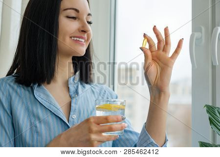 Woman Takes Pill With Omega-3 And Holding Glass Of Fresh Water With Lemon. Morning Picture Of House,