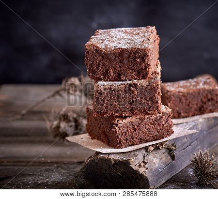 Stack Of Square Pieces Of Baked Brown Brownie Pie On A Gray Board, Black Background