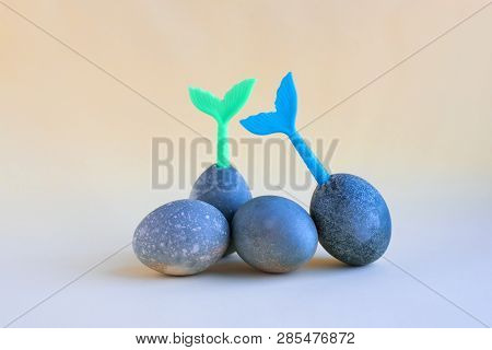 Four Blue Easter Eggs Lie On A Yellow Background. Blue And Green Tails Of Mermaids Stick Out Of Eggs