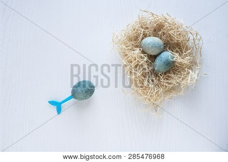 Easter Eggs Lie In A Nest On A White Wooden Background. Three Blue Eggs. Blue Tail Of Mermaid Stick 