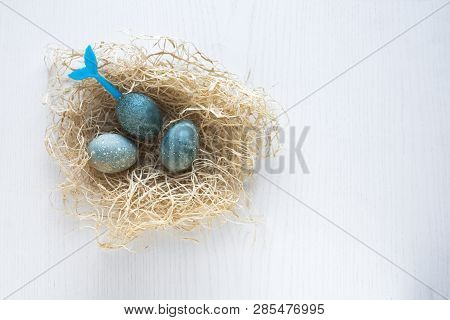 Easter Eggs Lie In A Nest On A White Wooden Background. Three Blue Eggs. Blue Tail Of Mermaid Stick 