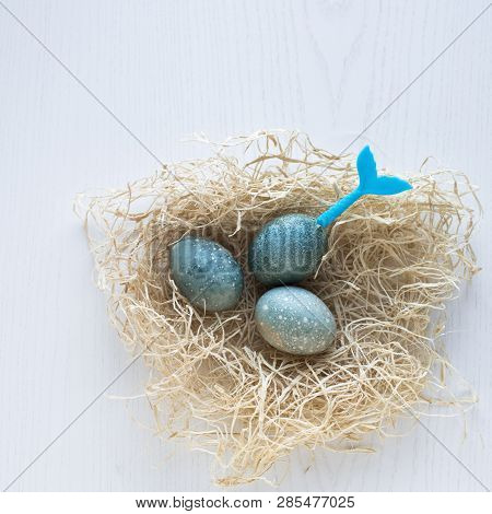 Easter Eggs Lie In A Nest On A White Wooden Background. Three Blue Eggs. Blue Tail Of Mermaid Stick 