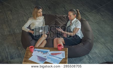 Two Beautiful Business Woman In Skirts Resting On The Couch, Holding A Laptop Girl, The Other Girl T