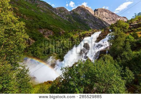 Waterfall And Rainbow On The Way To Briksdal Or Briksdalsbreen Glacier In Olden, Norway And Green Mo