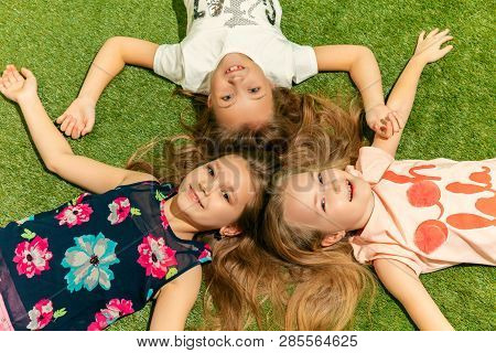 Group Of Happy Children Playing Outdoors. Kids Having Fun In Spring Park. Friends Lying On Green Gra