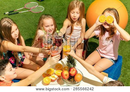Kids Fashion Concept. The Group Of Teen Boys And Girls Sitting On Green Grass At Park. Children Colo