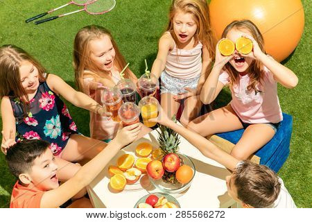 Kids Fashion Concept. The Group Of Teen Boys And Girls Sitting On Green Grass At Park. Children Colo