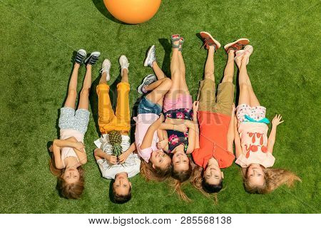 Group Of Happy Children Playing Outdoors. Kids Having Fun In Spring Park. Friends Lying On Green Gra