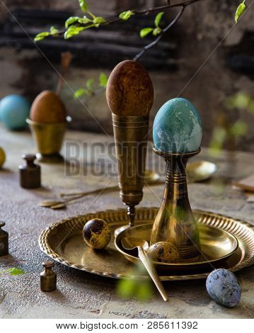 Easter Eggs Painted With Natural Dyes Standing On Brass Golden Stacks And Plate On Concrete Backgrou