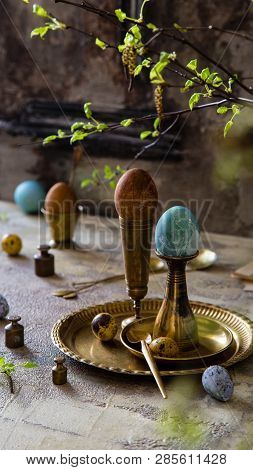 Easter Eggs Painted With Natural Dyes Standing On Brass Golden Stacks And Plate On Concrete Backgrou