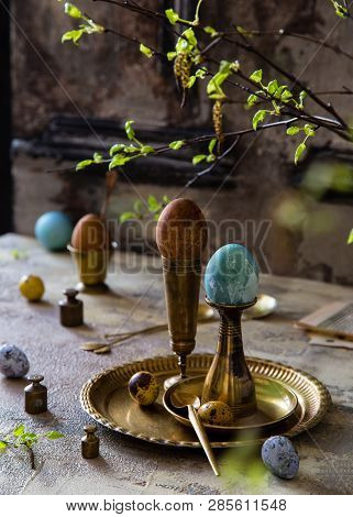 Easter Eggs Painted With Natural Dyes Standing On Brass Golden Stacks And Plate On Concrete Backgrou