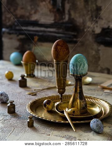 Easter Eggs Painted With Natural Dyes Standing On Brass Golden Stacks And Plate On Concrete Backgrou