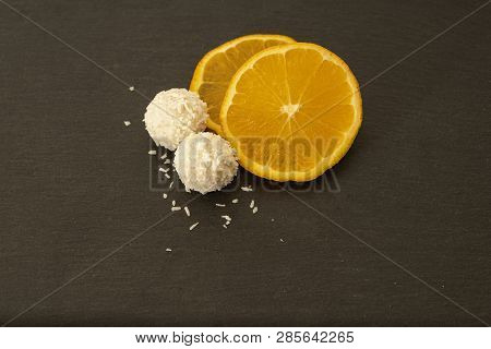 Rafaello Homemade Delicious Candy Sitting Next To Fresh Orange Slices. Sweer And Natural Snack