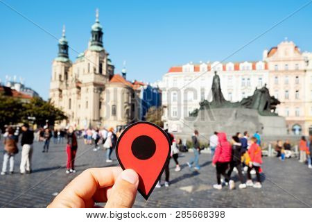 closeup of a young caucasian man with a red marker in his hand pointing the Old Town Square in Prague, Czech Republic, with the Saint Nicholas church and the Jan Hus Monument in the background