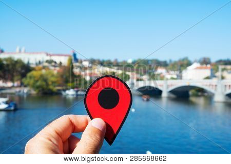 closeup of the hand of a caucasian man with a red marker pointing the Vltava River in Prague, Czech Republic, with the Manes bridge and the Prague Castle in the background