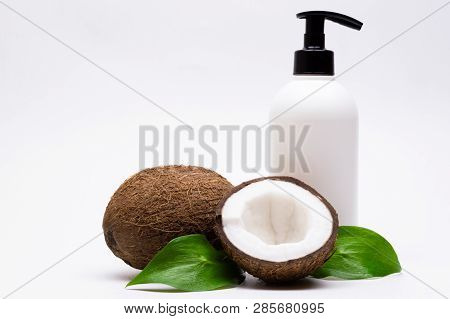 Natural Cosmetics Concept. Сoconuts, Green Leaves And White Plastic Body Cream Bottle. White Backgro