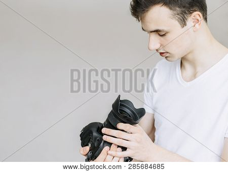 A Young Man Holds A Photo Camera And Looks At It. Isolated Gray Background