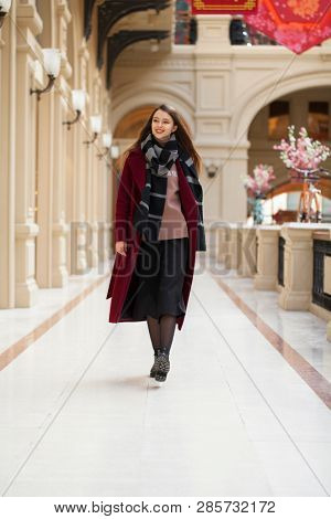 Full body portrait. Young beautiful woman in stylish in a long burgundy coat, indoor shop