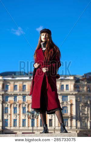 Full body portrait. Young beautiful brunette woman in stylish in a long burgundy coat walking in spring street