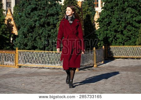 Full body portrait. Young beautiful brunette woman in stylish in a long burgundy coat walking in spring street