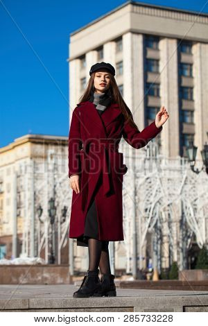 Full body portrait. Young beautiful brunette woman in stylish in a long burgundy coat walking in spring street