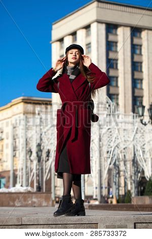 Full body portrait. Young beautiful brunette woman in stylish in a long burgundy coat walking in spring street