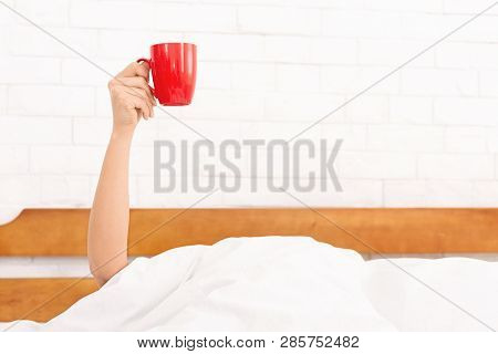 Drinking Coffee Early In Morning. Femaale Hand Raised Up Red Cup In Bed, Copy Space