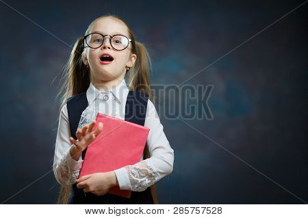 Caucasian Schoolgirl With Open Mouth Hold Book. Suprised Elementary School Girl In Glasses And Forma