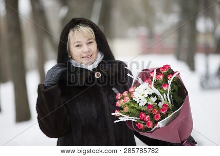 Woman In A Fur Coat With A Bouquet Of Flowers On A Winter Background