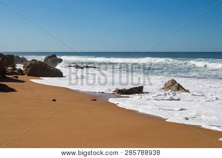 Rocks On The Clean Beach With Dark Yellow Sand. Foamy Waves Of The Atlantic Ocean. Horizon In The Ba
