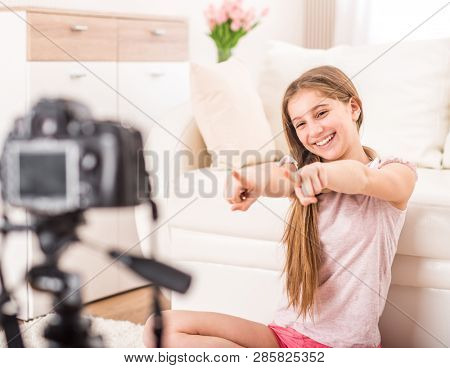 Young smiling videobloger teen girl is pointing at camera in living room
