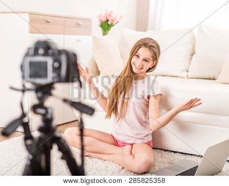 Young smiling videobloger teen girl is pointing at camera in living room