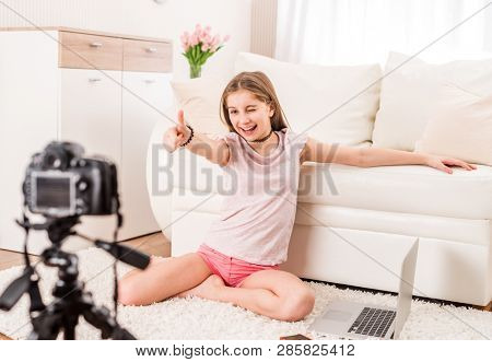 Young smiling videobloger teen girl is pointing at camera in living room