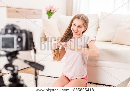 Young smiling videobloger teen girl is pointing at camera in living room