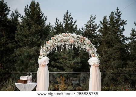 A Flower Arch With The Peach Curtains And A Little Table Near It. Forest At The Background.