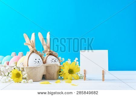 Easter Colored Eggs In Paper Tray With Decorationd On Blue Background
