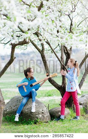 Happy Little Girls Outdoors Rehearsal With Guitar And Singing In Blossom Spring Park
