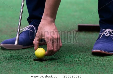 Minigolf Player Pulls A Yellow Ball Out Of The Hole, Close-up