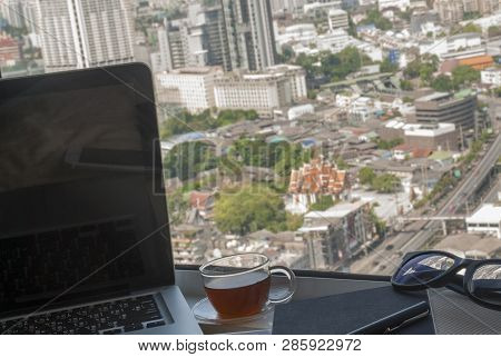 The Work Area By The Window Has A Laptop With A Book, Pen, Glasses, Tea And City Views.