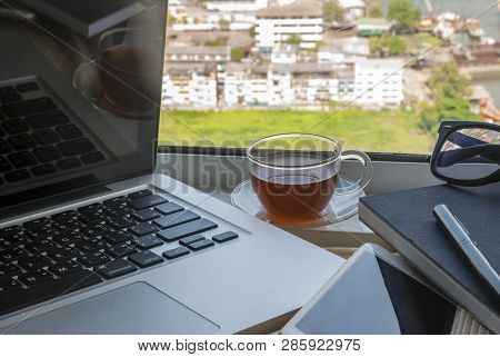 The Work Area By The Window Has A Laptop With A Pen Nofebook And A City View.