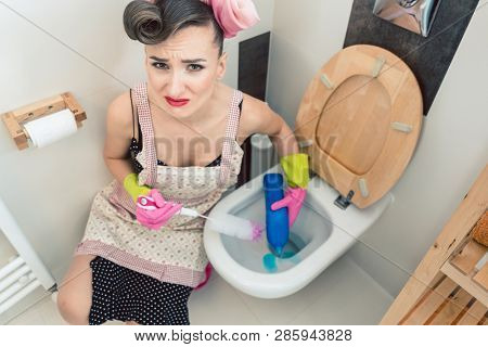 Homemaker having perfectly no fun at all cleaning the restroom with brush and household detergent