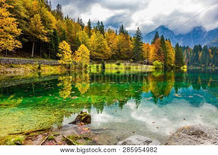 Fantastically autumn forests are reflected in the water. The quiet lake in Northern Italy, Lago de Fusine. Concept of cultural and ecological tourism. High water of the lake after a rain