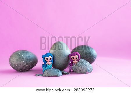Three Gray, Blue Easter Eggs, Like Stones. Two Toy Mermaids. Lilac Background