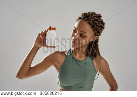 Healthy Products For Sportsmen. Young Mixed Race Fitness Woman In Sportswear Holding Bottle With Spo